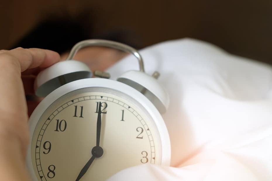 A close-up of a hand reaching for a ringing alarm clock, symbolizing waking up in the morning.