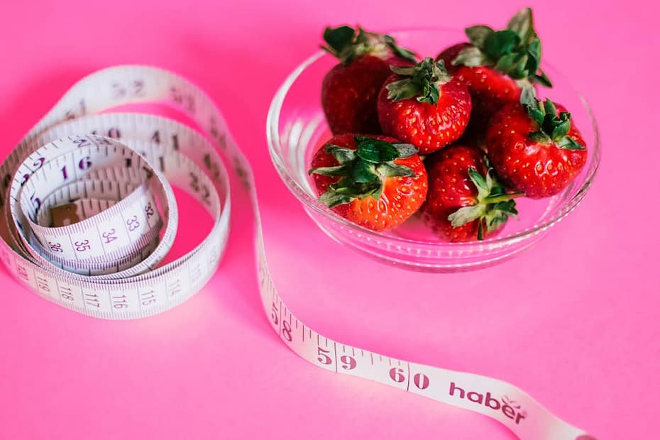 A glass bowl of fresh strawberries paired with a pink measuring tape symbolizes healthy eating.