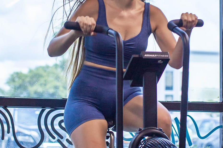 Young woman enjoying a vigorous workout on a stationary bike indoors with a vibrant, motivating atmosphere.