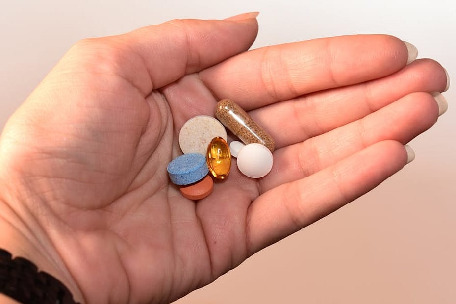 A close-up image of a human hand holding assorted pills, showcasing diverse colors and shapes.