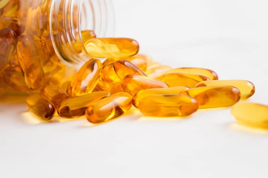 Close-up of fish oil capsules spilling from a bottle on white background.