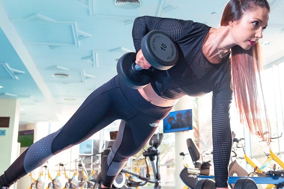 Woman performing a plank row with dumbbells in a bright Dubai gym.