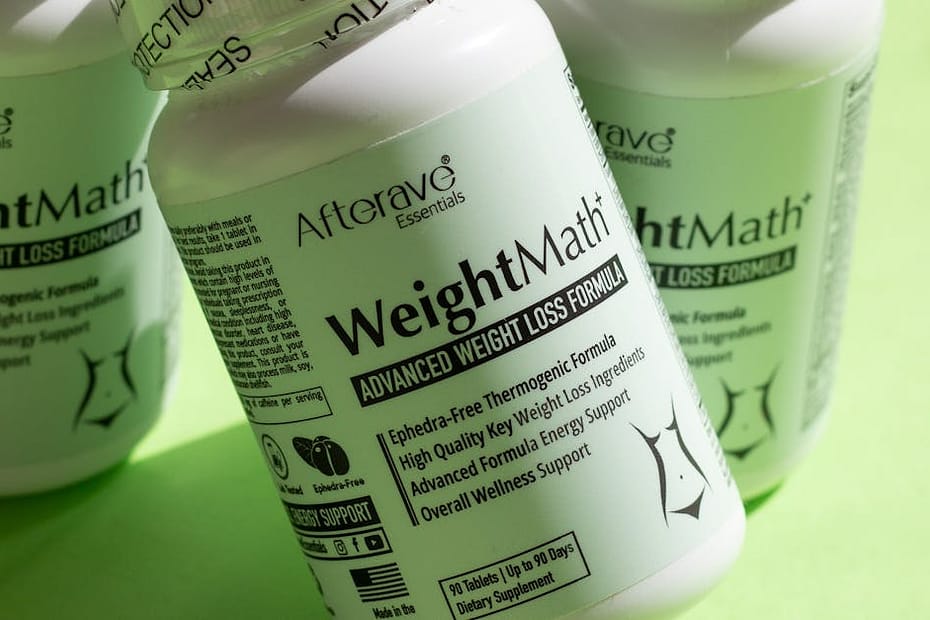 Three bottles of weight loss supplements with tablets on a green surface.