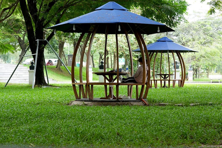 Outdoor park scene with a person seated in a wooden pavilion under a blue roof.