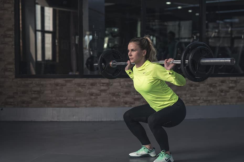 Dedicated woman in neon activewear performs a weighted squat in an indoor gym setting.
