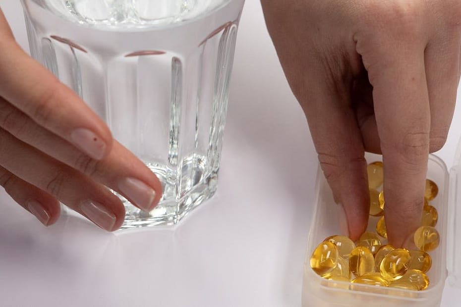 A hand selecting supplements from a pill box beside a glass of water, symbolizing health.