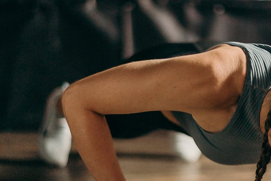 Fit woman doing a dumbbell push-up in a gym, highlighting strength and fitness training.