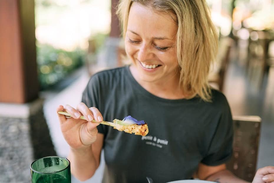Woman smiling while enjoying a meal in a casual restaurant setting with natural light.