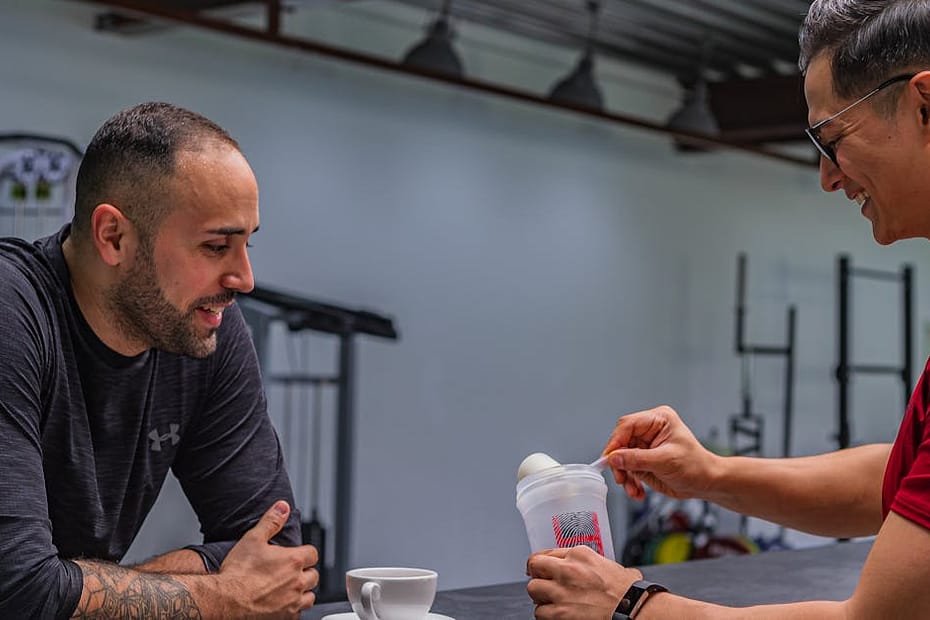 Side view of strong friends talking while preparing high protein smoothie after hard workout