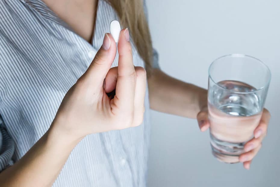 Close-up of a woman holding a pill and a glass of water, ready to take medication.