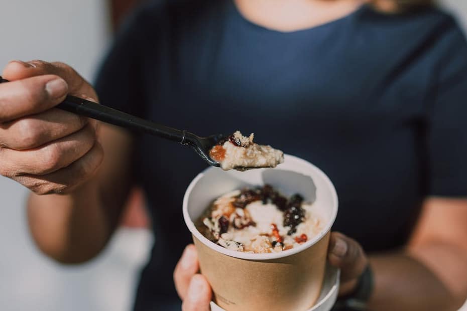 Close-up of a person holding a bowl of vegan oatmeal topped with fruits.