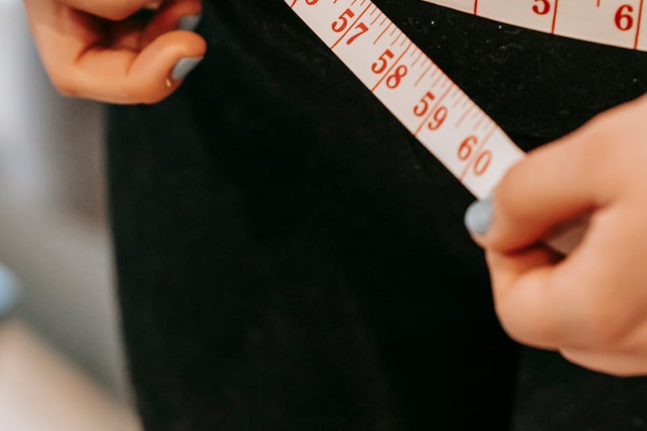 From above of crop anonymous plump female using measuring tape around hips in gym