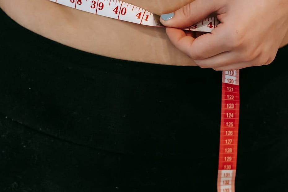 A woman measures her waist using a red measuring tape while wearing activewear.