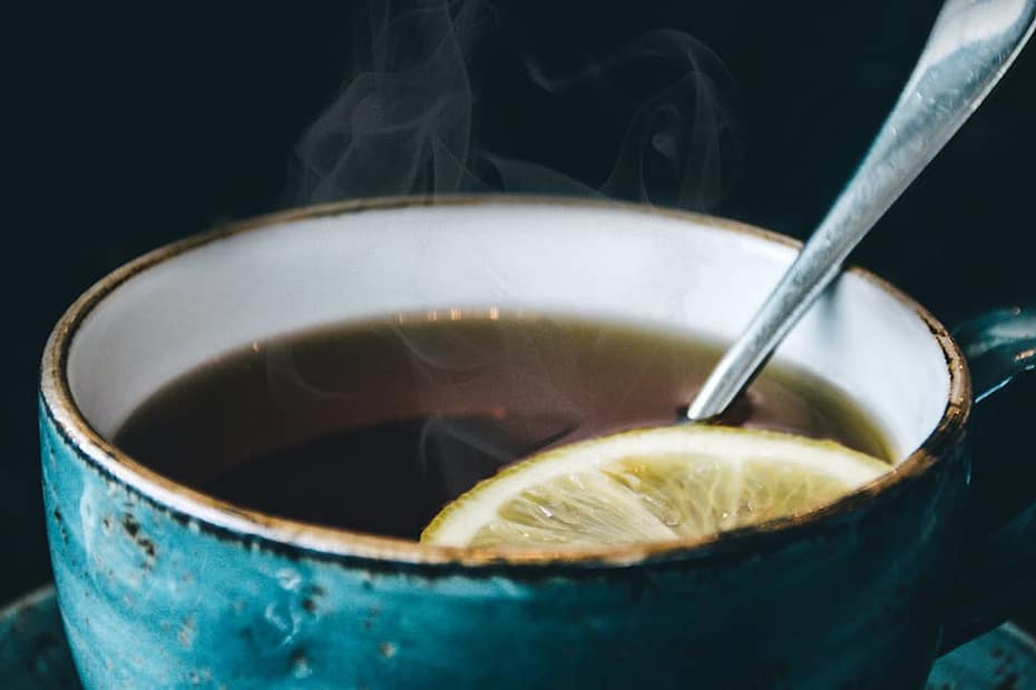 Close-up of aromatic steaming lemon herbal tea served in a ceramic cup with saucer.