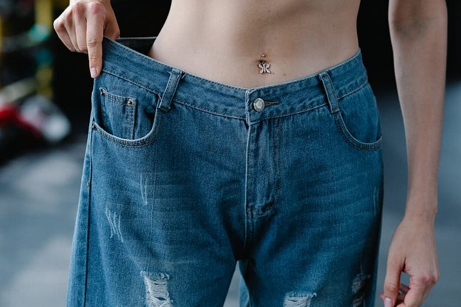A woman showcases significant weight loss results confidently wearing loose jeans.