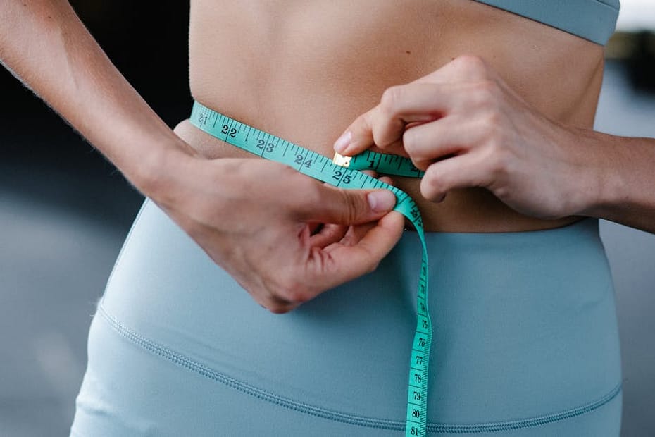 Close-up of a woman measuring her waist with a tape in a fitness setting.