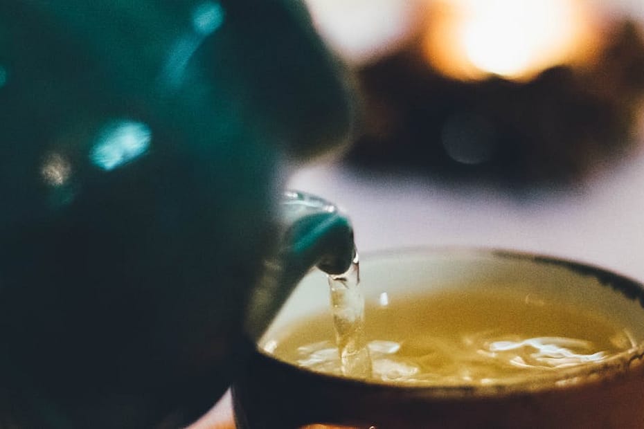 Warm close-up image of tea being poured into a teacup with blurred background ambiance.