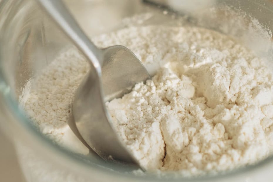 A close-up of a glass jar filled with flour and a metal spoon, ideal for baking themes.