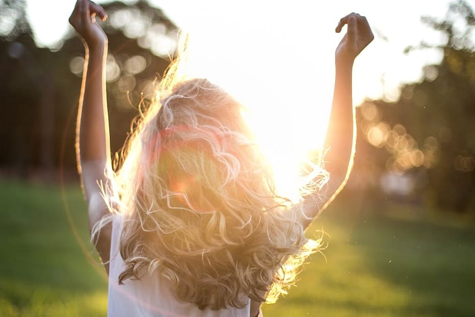 A woman with outstretched arms celebrates the sunset in a grassy field, capturing the essence of freedom and joy.