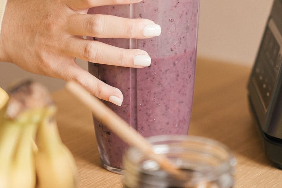 Person blending fresh fruit smoothie in a container with a lid next to bananas and honey.