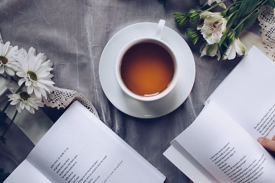 Inviting cozy reading setup with tea, poetry books, and fresh flowers on a table.
