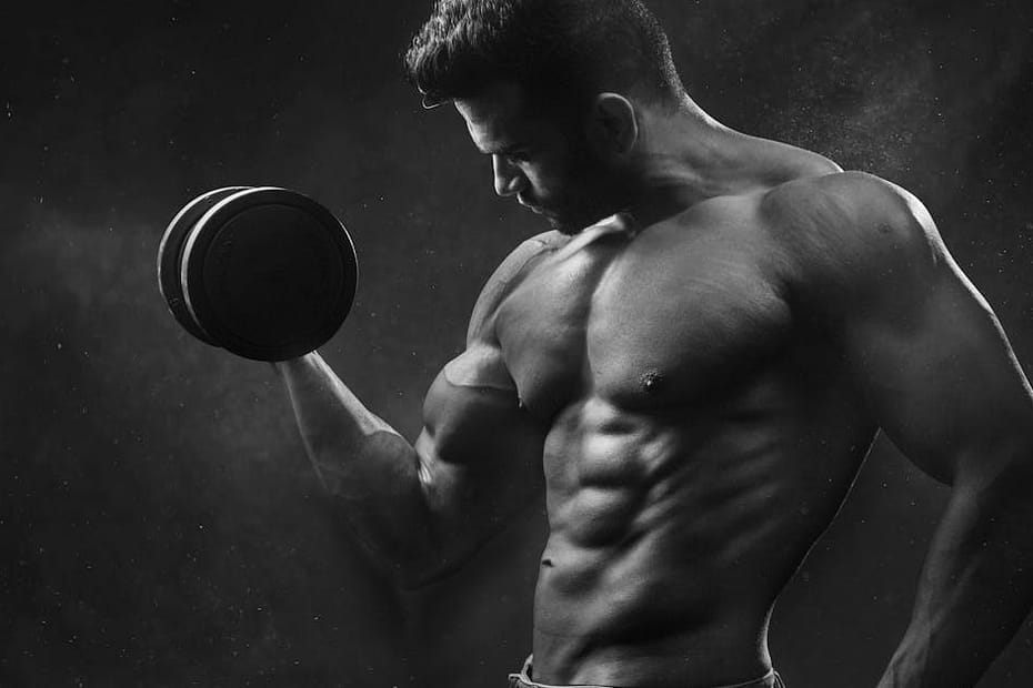 Powerful black and white portrait of a shirtless bodybuilder lifting dumbbells in the gym.