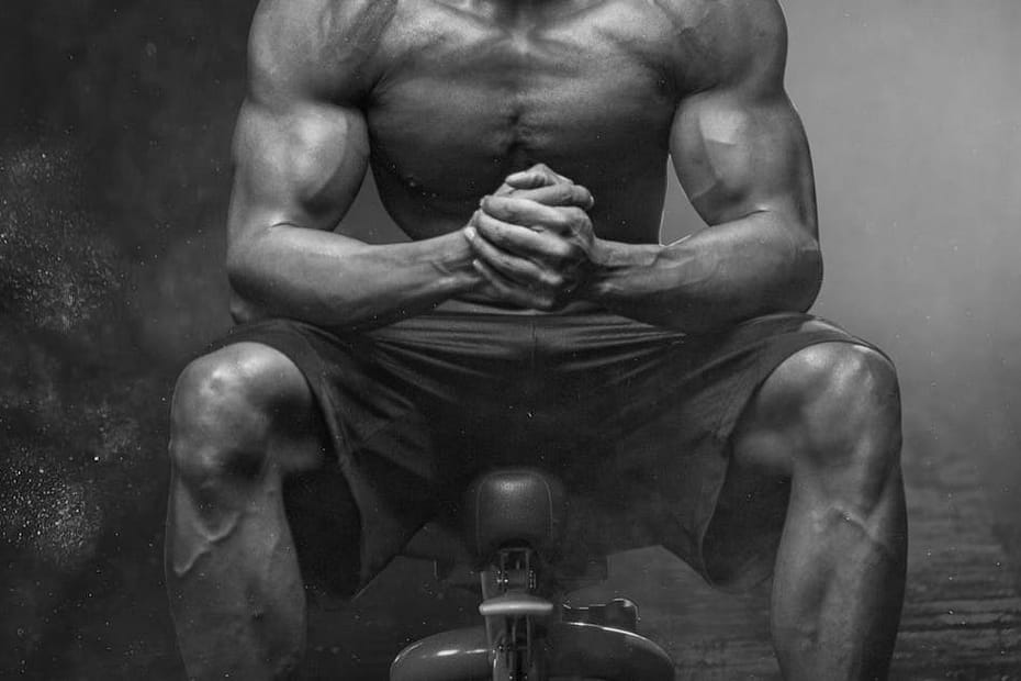 A powerful bodybuilder sitting with intense focus, showcasing muscular definition and strength.