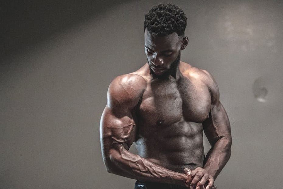 A strong, shirtless male bodybuilder showcasing muscles and strength in a gym setting.
