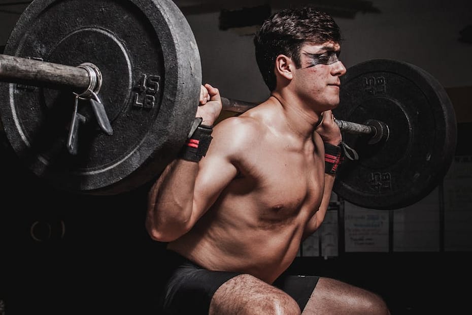 Shirtless man performing a barbell squat, showcasing strength and fitness.