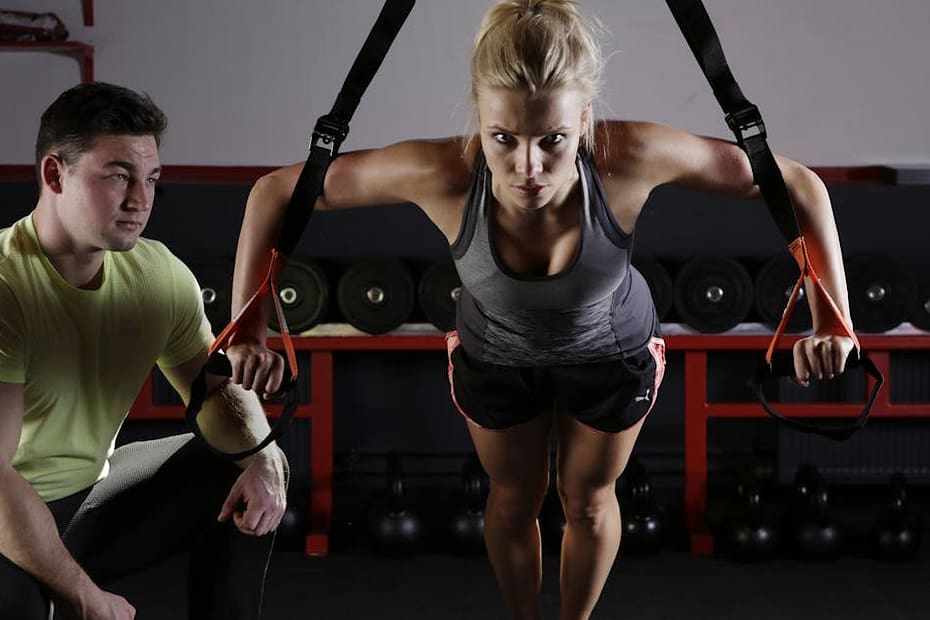 A woman performing strength training with a trainer in a gym setting, showcasing fitness and dedication.