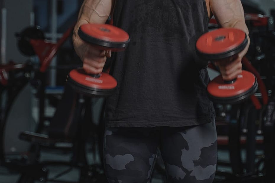 Strong man lifting dumbbells in a gym, showcasing fitness and muscle strength.