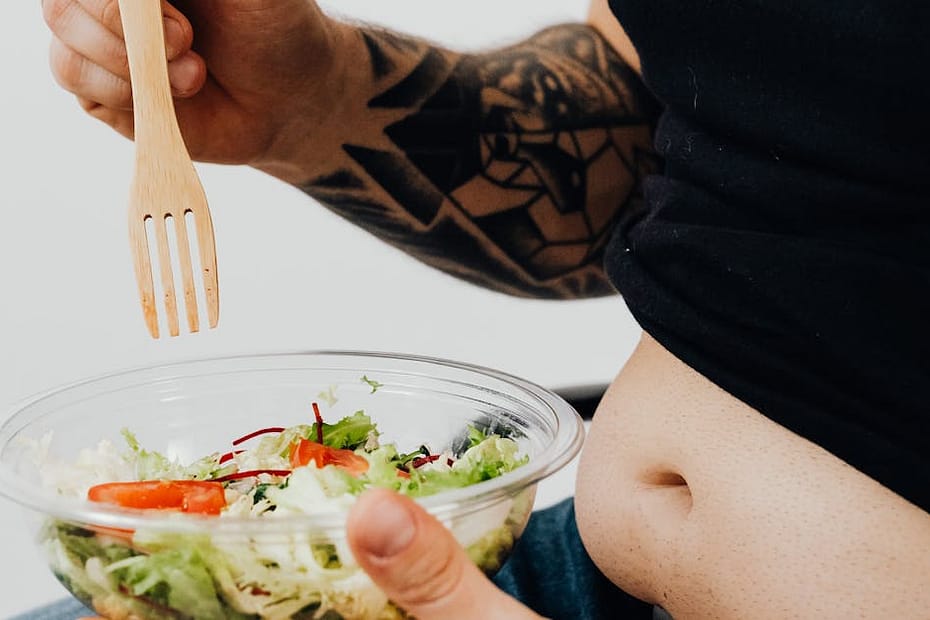 Person holding a bowl of salad with visible tattoos, highlighting healthy eating with personal style.