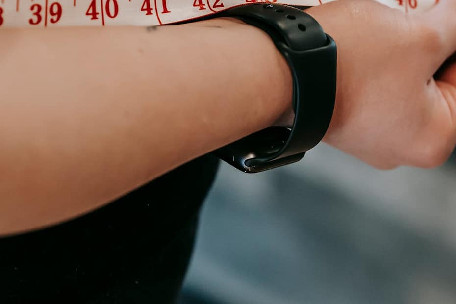 Crop anonymous female with measuring tape around big belly on blurred background of gym