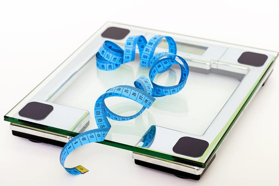 A digital glass weighing scale with a blue measuring tape, symbolizing weight management.