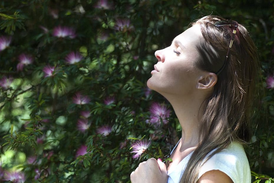 A woman enjoying a serene moment in a sunlit garden, surrounded by vibrant flowers.