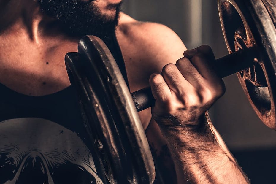 Bearded man in gym lifting a heavy dumbbell, showcasing strength and fitness.