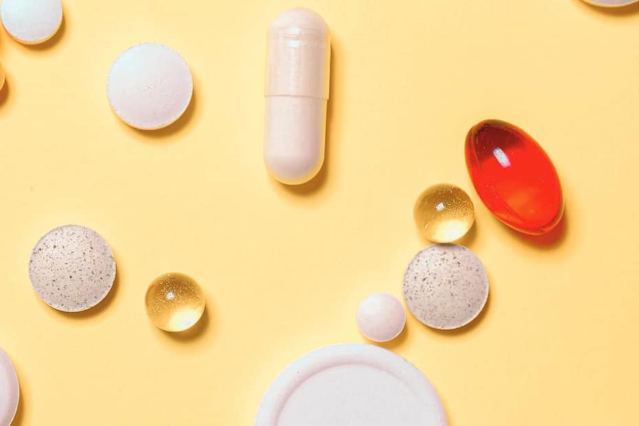 Colorful assortment of pills and capsules on a vibrant yellow background.