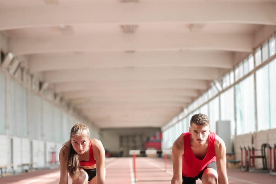Couple of professional sportspeople ready for sprinting on empty track in training hall on sunny day