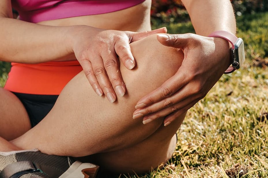 Close-up of a woman sitting cross-legged on grass, holding her knee, wearing a smartwatch.