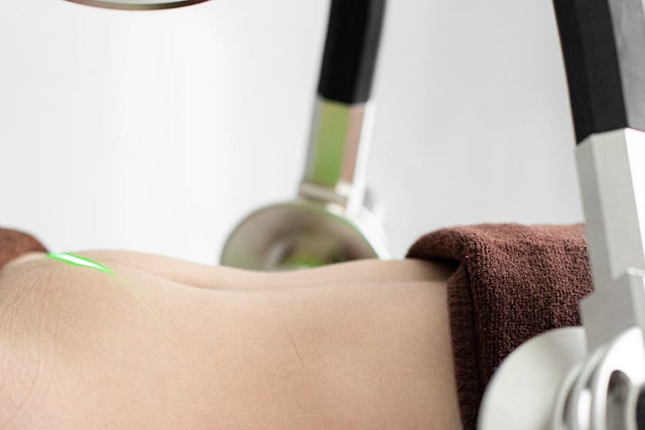 Crop faceless female client lying under modern laser weight loss machine with heads during treatment in modern light medical clinic